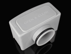 Afbeelding van een grijze sanitaire aansluiting met de tekst 'OPEN & CLEAN' en een pijl die de richting aangeeft om te openen. Het apparaat heeft een rubberen afdichtring