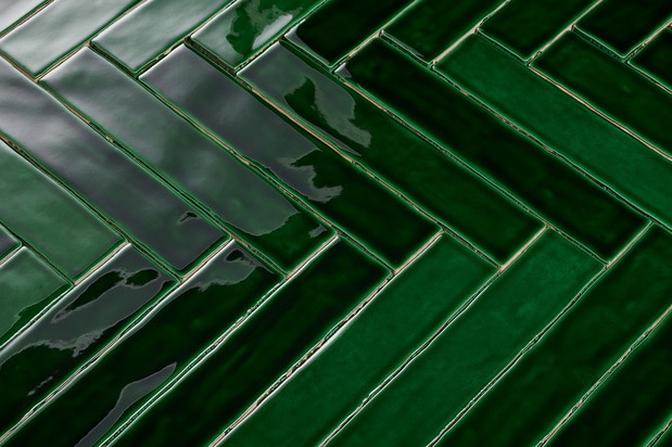 Close-up van rechthoekige, glanzende, donkergroene tegels, gerangschikt in een visgraat patroon.