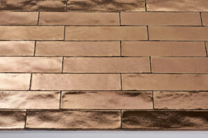 Afbeelding van glanzende, rechthoekige tegels in een koperkleurige tint, gelegd in een horizontaal patroon.