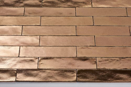 Afbeelding van glanzende, rechthoekige tegels in een koperkleurige tint, gelegd in een horizontaal patroon.