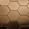 Wandtegel Hexagon Onda goud Close-up van zeshoekige, brons/ gouden tegels met een matte afwerking, gerangschikt in een honingraatpatroon.