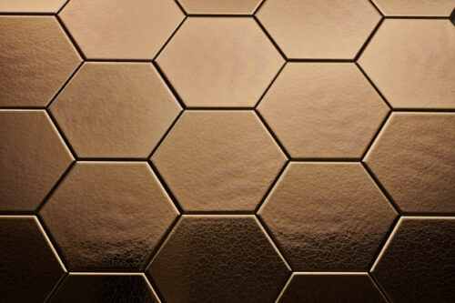 Wandtegel Hexagon Onda goud Close-up van zeshoekige, brons/ gouden tegels met een matte afwerking, gerangschikt in een honingraatpatroon.