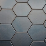 Wandtegel Hexagon Onda platinum Close-up van zeshoekige, donkergrijze tegels met een matte afwerking, gerangschikt in een honingraatpatroon.