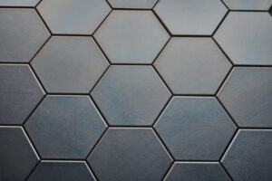 Wandtegel Hexagon Onda platinum Close-up van zeshoekige, donkergrijze tegels met een matte afwerking, gerangschikt in een honingraatpatroon.