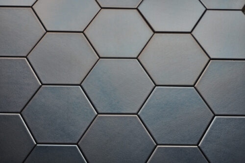 Wandtegel Hexagon Onda platinum Close-up van zeshoekige, donkergrijze tegels met een matte afwerking, gerangschikt in een honingraatpatroon.